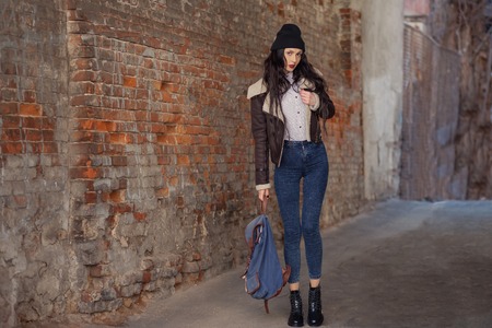 Outdoor lifestyle portrait of pretty young girl, wearing in hipster swag grunge style on urban background. Wearing hat and jeans with backpack. Spring fashion woman.の写真素材