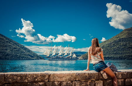 Beautiful young woman looking and waiting for amazing white sailboat at the seacoast.の写真素材
