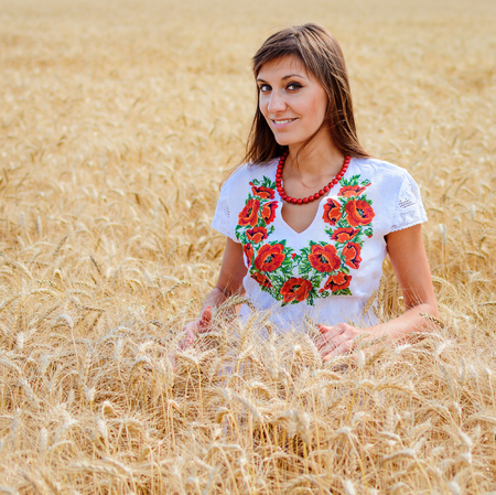 Beauty girl outdoors on the wheat field, woman dressed in national dress. Blowing long hair.の写真素材