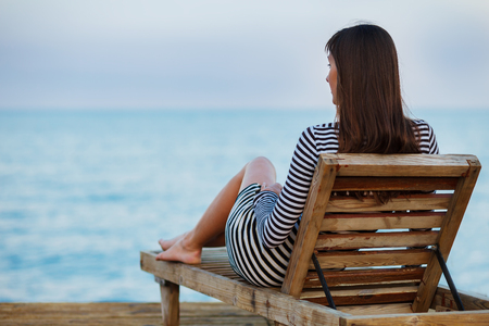 Outdoor portrit of beautiful young woman relaxing at the seacoast at the eveningの写真素材
