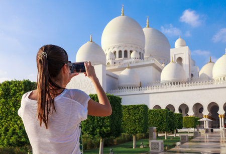 Young tourist woman shooting on mobile phone Sheikh Zayed great white mosque in Abu Dhabi, United Arab Emirates, Persian gulfの写真素材