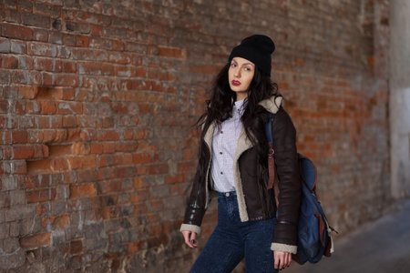Beautiful brunette girl in a beret and jeans with a backpack in the city.の写真素材