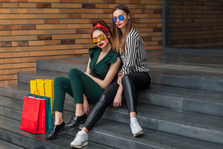 Portrait of two beautiful young women with shopping bags sitting on stairsの写真素材
