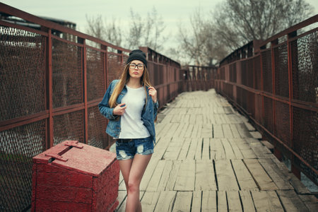 Beautiful girl in a denim jacket with a suitcase on the bridgeの写真素材