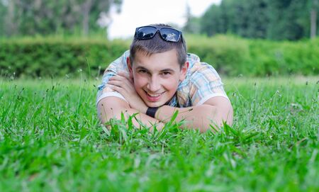 The young guy smiles broadly lying on a green lawnの写真素材