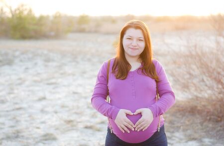 Young beautiful pregnant woman on a background sunset. 9th month of pregnancy.
