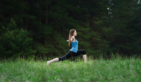 Young girl practicing yoga in nature in the woods on a background of green trees and grass.の写真素材
