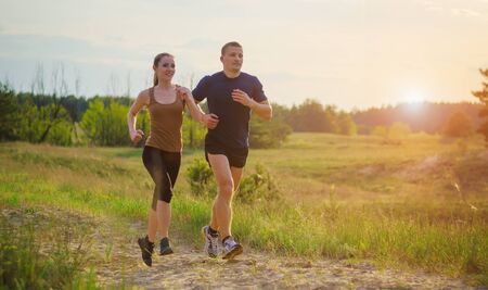Young couple running at sunset outdoors. Solar flare illuminates a couple back.