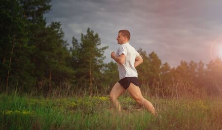 Young muscular man jogging outdoors, in the woods. Solar flare from sunsetの写真素材