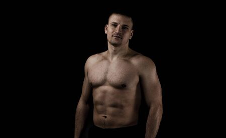Young muscular man on a black background. Hard light, dark lighting