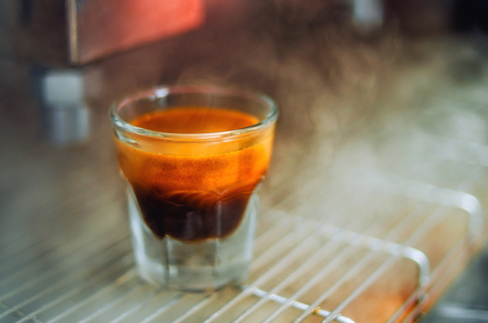 Cup of the espresso in the grid of coffee machine in a hot pair. Beautiful background.の写真素材
