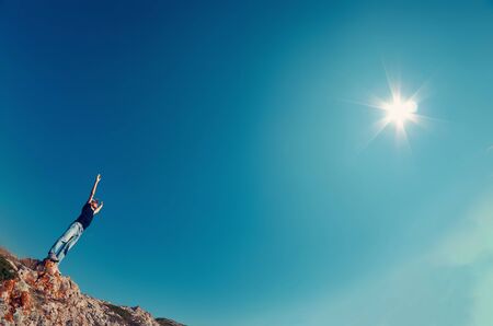 Young man  in jeans and black shirt on a mountain raised their hands to sky towards the sun....