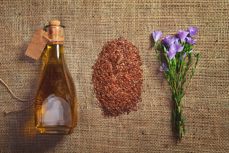 Flax flower, seeds and butter in a glass old bottle with a vintage cardboard label, on a brown burlap texture, Top viewの写真素材