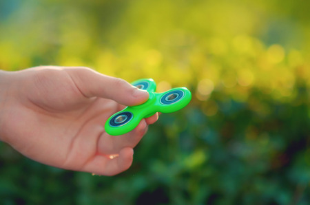teenager hand holding  trendy popular gadget fidget spinner. Man playing with green spinner outdoors  on the bright bokeh. Shallow DOF.の写真素材