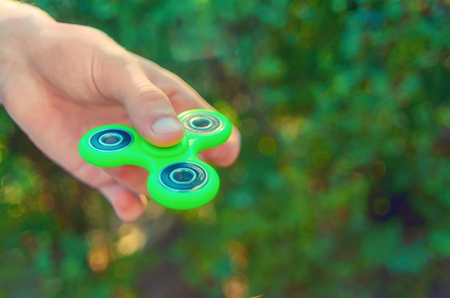 teenager hand holding  trendy antistress gadget fidget spinner. Man playing with green spinner outdoors  on the bright bokeh. Shallow DOF.の写真素材