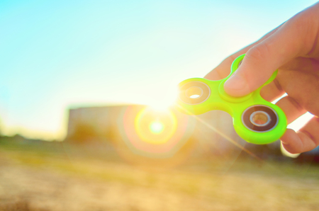Teenager hand holding  trendy antistress gadget fidget spinner. Man playing with green spinner outdoors on the bright bokeh sunlight rays. Shallow DOF.の写真素材