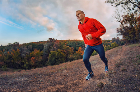 A athleticr jogger in a black leggins and shirt  runs on the colorful red autumnal forest hill with sunset dramatic sky. Photo show  active healthy lifestyle.の写真素材