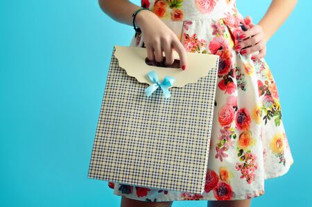 Close up female hands holding a stylish carton shopping bag. Conceptual studio photo isolated on the blue background.の写真素材