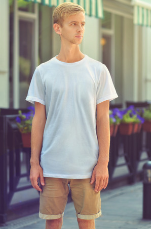 Urban template of clothes. Young  man stand on  a cozy stylish cafe with flowers  in a blank T-shirt and brown shorts.  Shallow DOF. Mockup can use for  you showcase.の写真素材