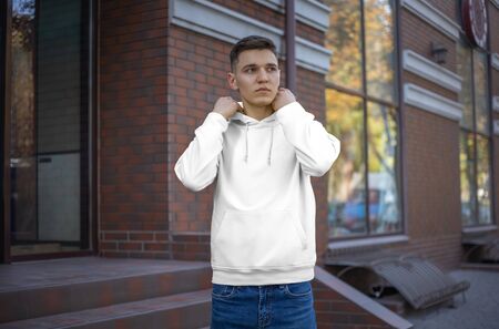 Template of a white hoodie on a young guy, front view. Presentation of fashionable clothes on the street. Mockup hoods for advertising in the store. Design casual man clothing.の写真素材
