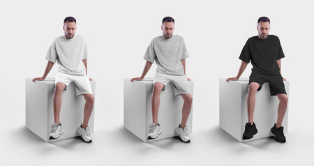 Mockup of white, black and gray men's oversized t-shirt with shorts on a man sitting on a cube....