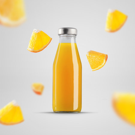 Mockup of a glass bottle with orange juice, transparent packaging with flying pieces of fruit....