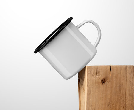 Template of white metal mug with black rim, handle, on edge of old beam, iron cup on board, isolated on background. Mockup of stylish enamel mug on timber, for design, branding, pattern, advertisingの写真素材
