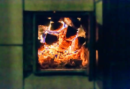 Beautiful old fireplace with light flame fire for heating building room, old fireplace consisting of thick oak wooden logs in hot flame fire, bright flame fire in old iron fireplace from slice treeの写真素材