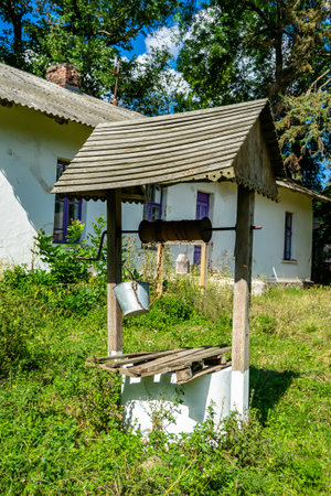Old well with iron bucket on long forged chain for clean drinking water, photography consisting of old rounded well with roof, clear water in big bucket, spring water at aluminum bucket from old wellの写真素材