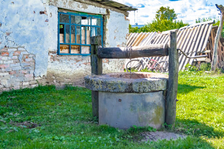 Old well with iron bucket on long forged chain for clean drinking water, photography consisting of old rounded well with roof, clear water in big bucket, spring water at aluminum bucket from old wellの写真素材