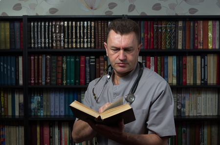 the doctor stands with a book in the libraryの写真素材