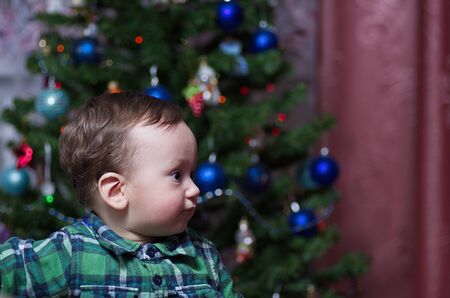 A little boy in a green shirt stands at a festive Christmas treeの写真素材