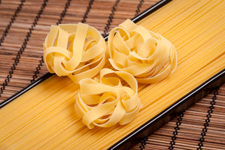 Unboiled tagliatelle and spaghetti on a rural matの写真素材
