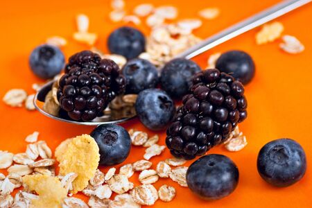 Muesli, corn flakes, blackberries and blueberries on a bright orange backround. Selective focus.の写真素材