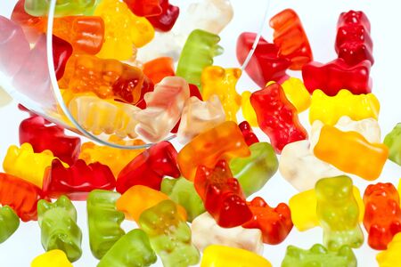 A pile of multicolored gummy bears in a crystal glass and ona a bright lit white background. Selective focus.の写真素材