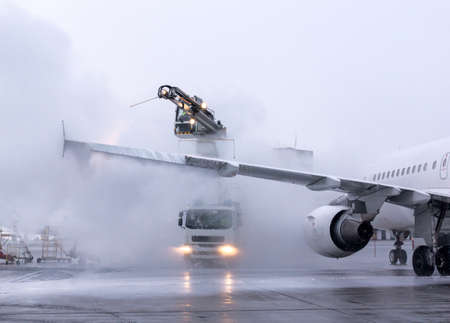 De-icing procedure for big airliner at the international airport. Winter, overcast, cold weather. Large clouds of steam. Jets of sprayer. Special airfield equipment. Ice prevention. Aviation safety.の写真素材