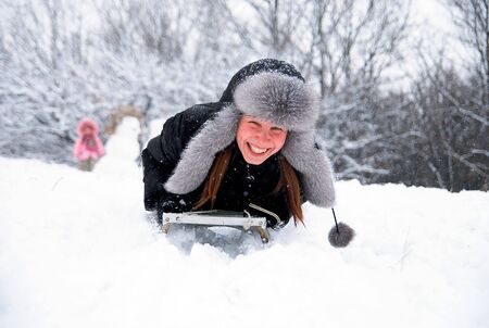 laughing girl in winter clothing goes down on sleds down the hillの写真素材