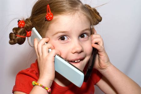little girl talking on two mobile phones and looks at cameraの写真素材