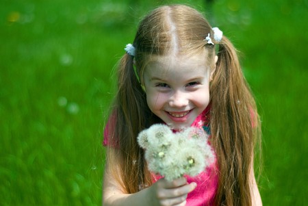 smiling little girl on a green meadow with a bouquet of dandelionsの写真素材