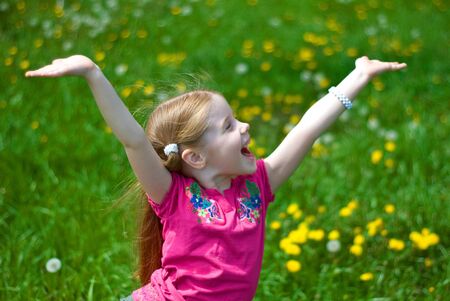 laughing little girl on a green meadow with dandelionsの写真素材