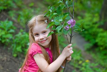 smiling nice little girl holding lilacs at the trunkの写真素材