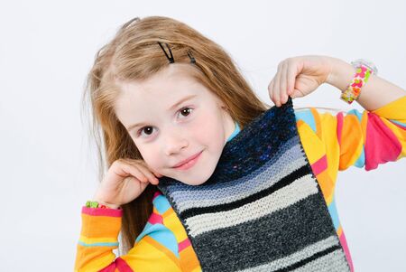 studio shot of pretty little girl trying on knitted scarfの写真素材