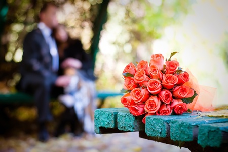 bridal bouquet of red roses on a green meadow and blurred newlywedsの写真素材