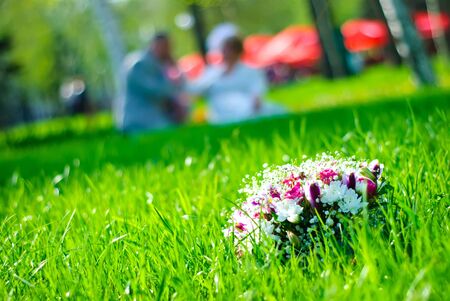 Bridal bouquet on a green meadow and blurred newlywedsの写真素材