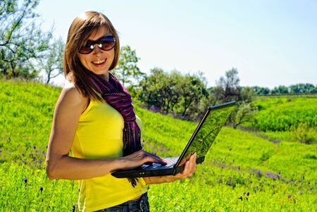 Smiling beautiful woman with laptop outdoor. Sunny summer day.の写真素材