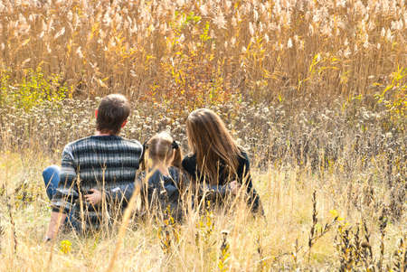 Mother, father and daughter sitting at the meadow in autumnの写真素材