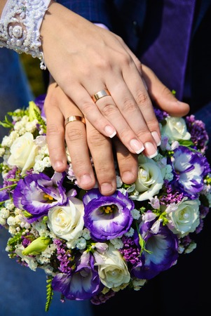 Hands of the groom and the bride with wedding rings on top of the bride's bouquetの写真素材