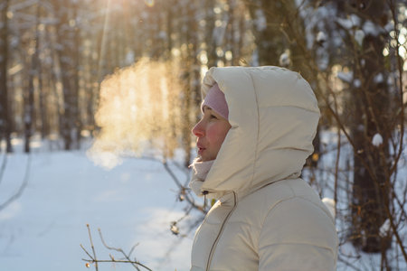 Young beautiful woman breathing steam in winter sunny forestの写真素材