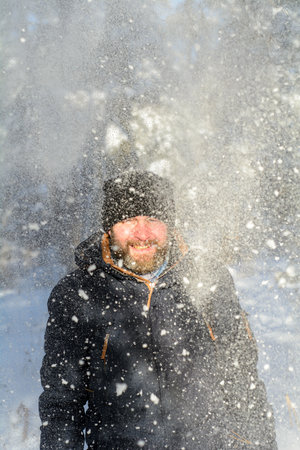 A frozen bearded man in warm clothes stands under the snow in a winter sunny forestの写真素材