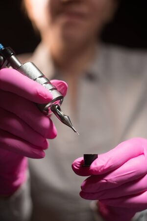 close-up female hands dipping paint tattoo machineの写真素材